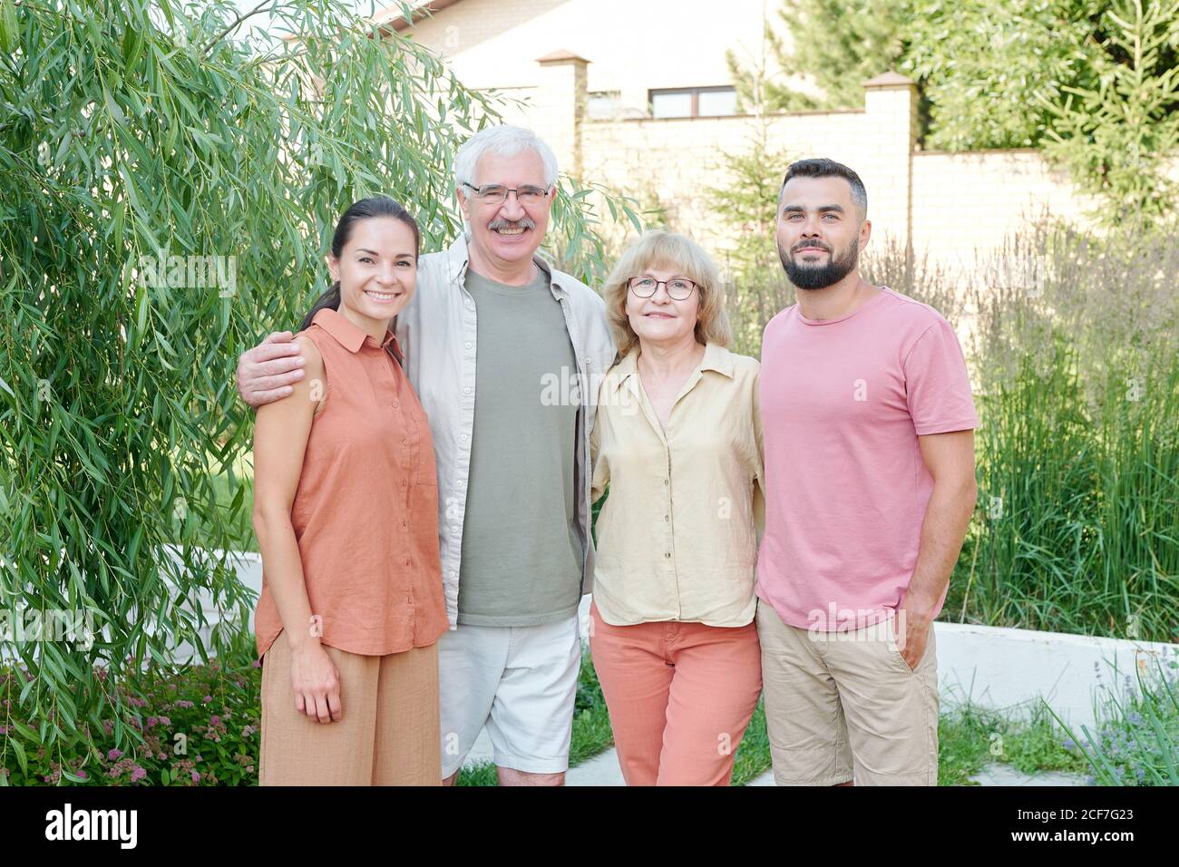 Medium long shot family portrait of senior parents and their young adult children standing together outdoors on summer day looking at camera Stock Photo