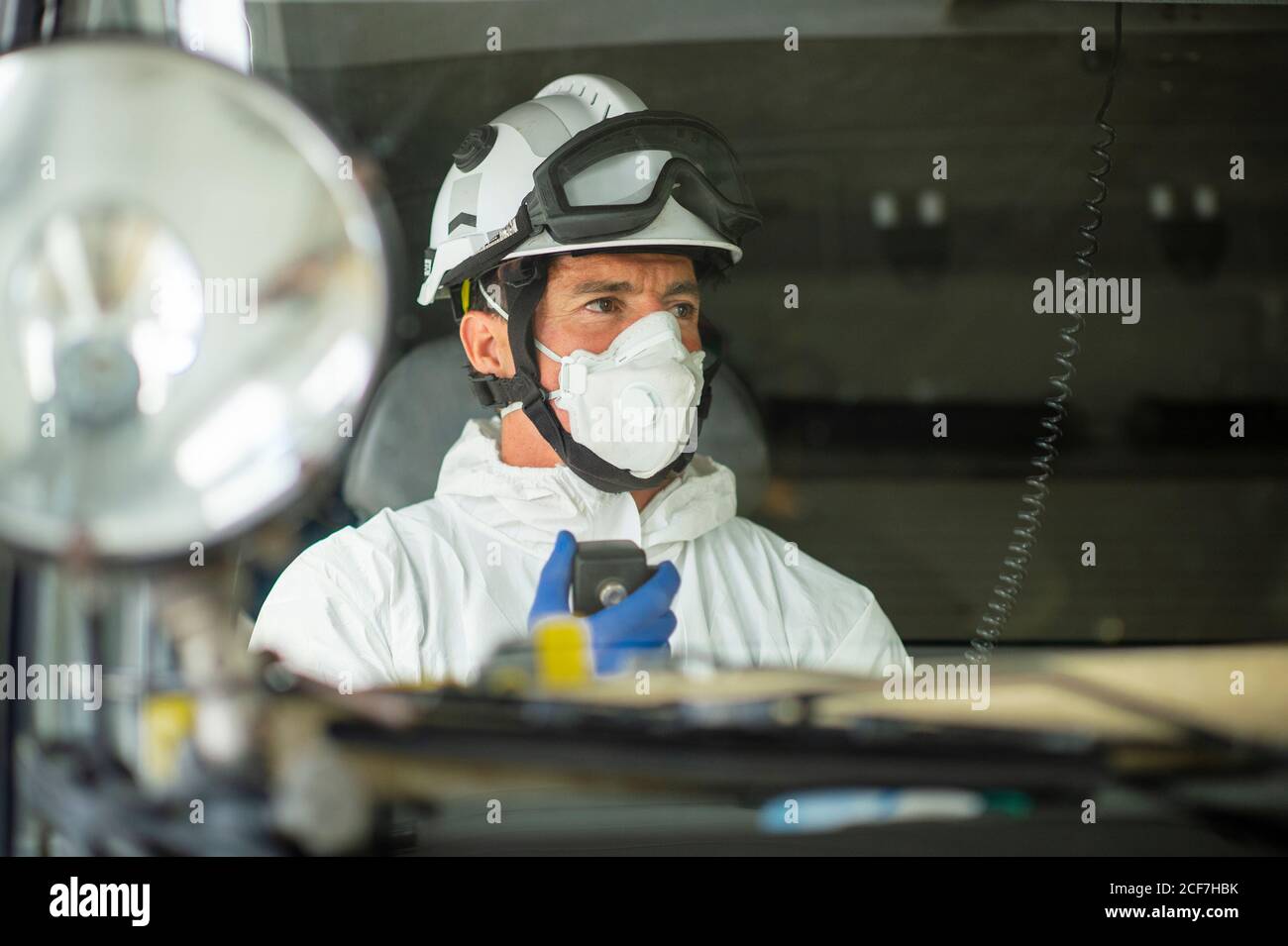 Firefighter wearing respirator and helmet sitting in fire car and using walkie talkie Stock Photo