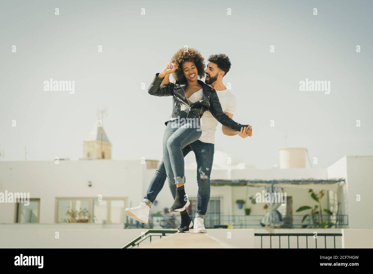Multiracial man and Woman laughing and balancing on wall while having fun on city street during date Stock Photo