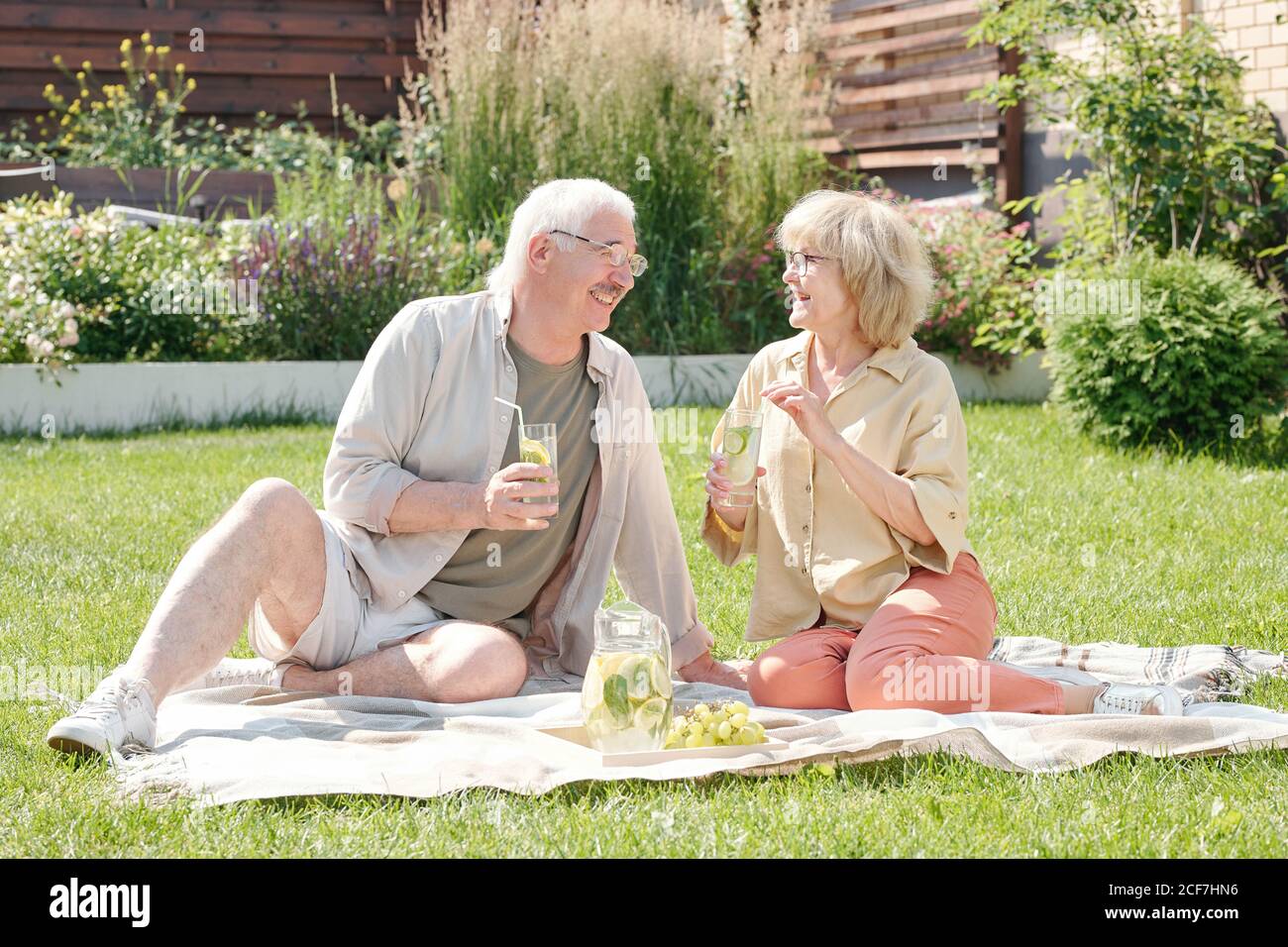 Senior man and his lovely wife sitting on lawn in backyard drinking fresh lemonade and chatting Stock Photo