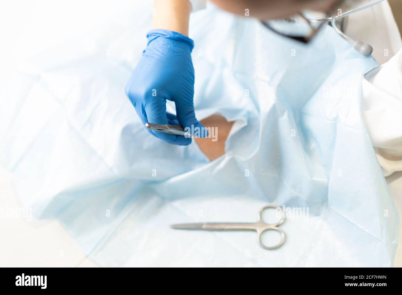 Young female doctor in uniform and medical mask taking out stitches from crop hand of Woman in napkin Stock Photo