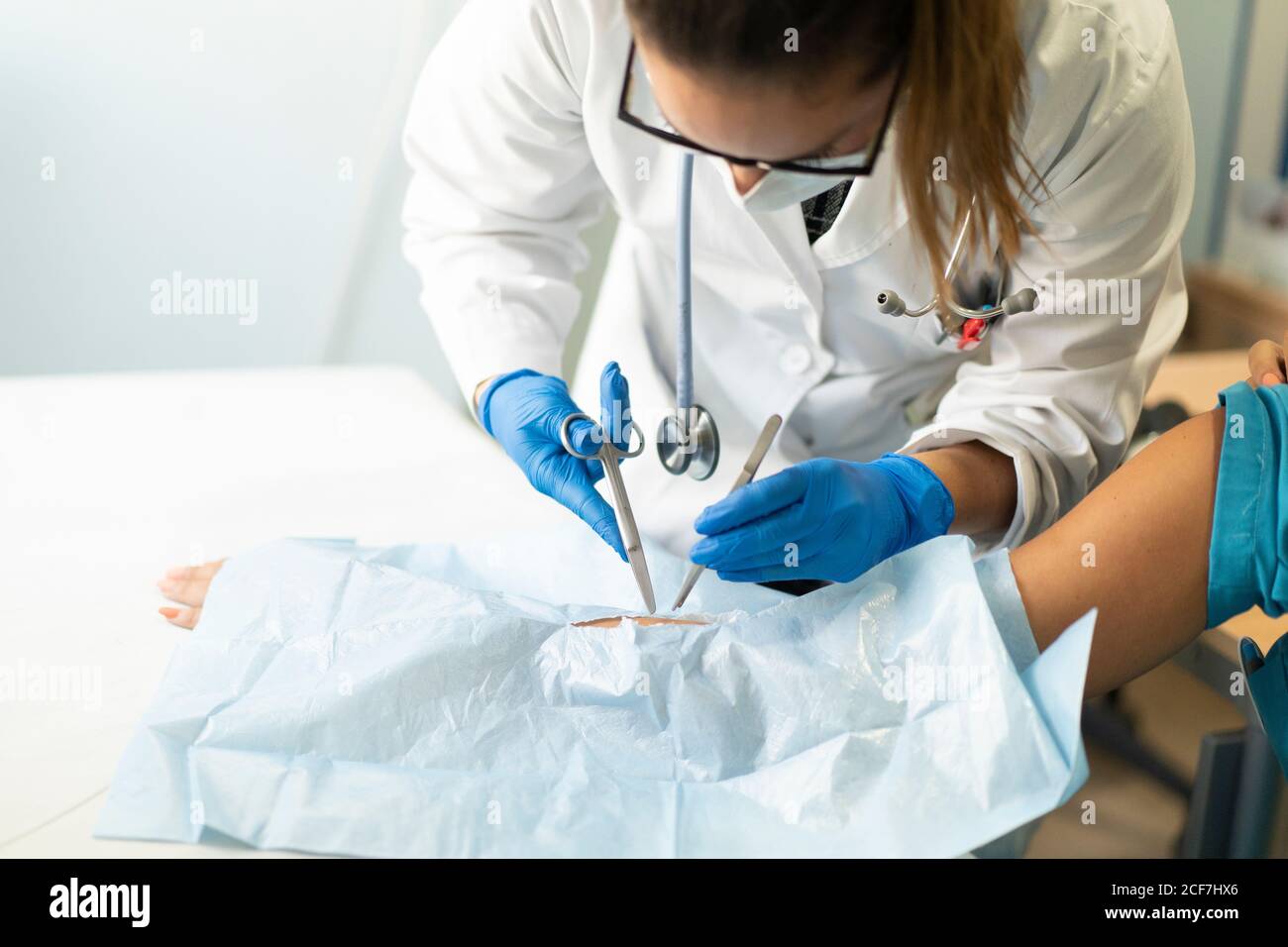 Young female doctor in uniform and medical mask taking out stitches from crop hand of Woman in napkin Stock Photo
