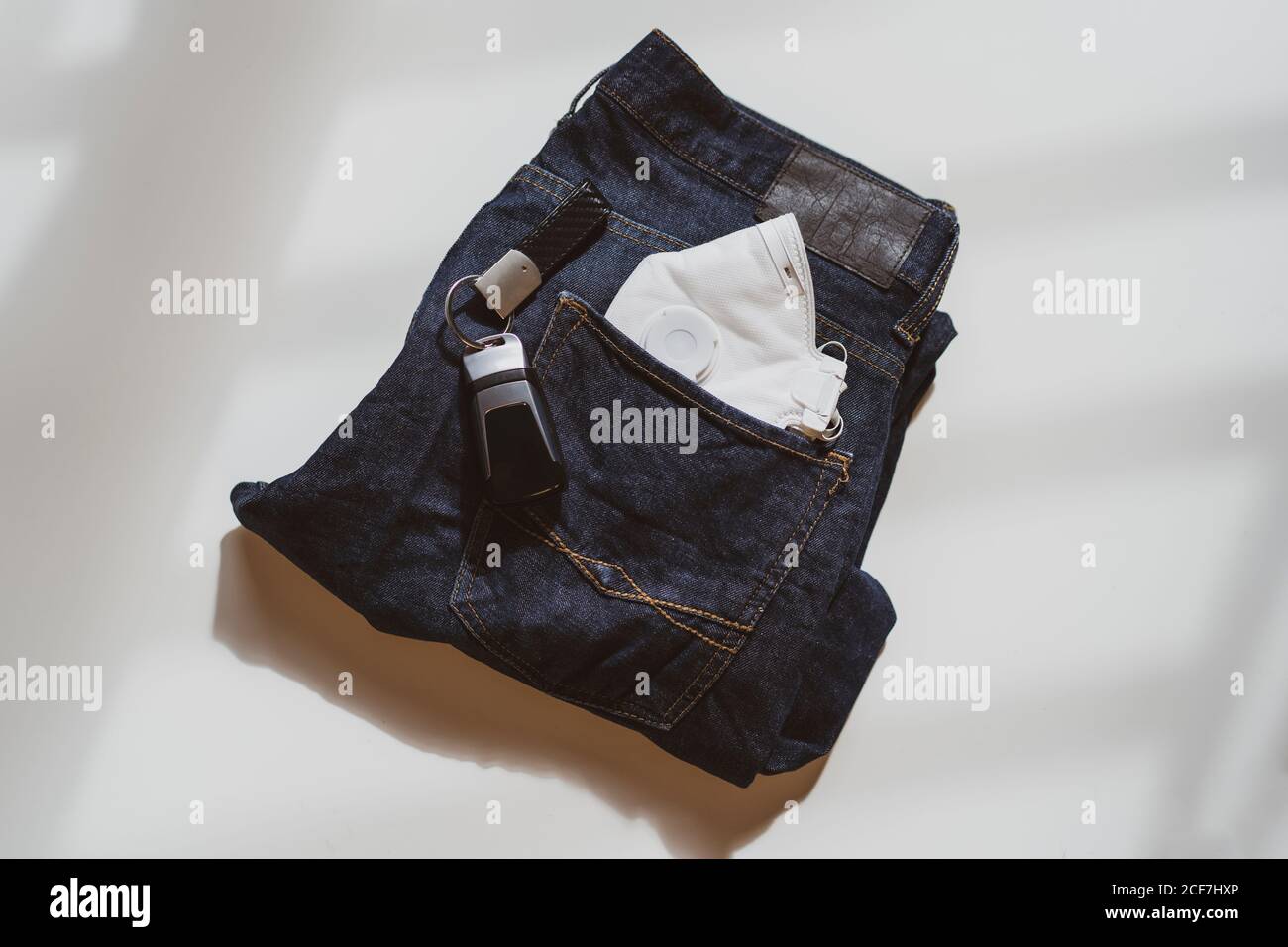 From above of folded jeans with white protective mask in pocket and car keys placed on white background in light studio Stock Photo