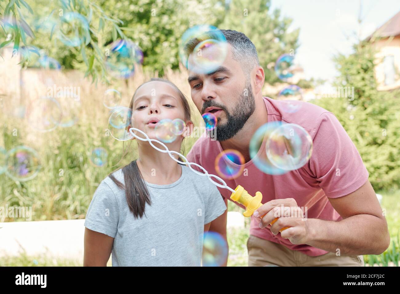 Joyful father having fun with his lovely daughter blowing soap bubbles outdoors Stock Photo