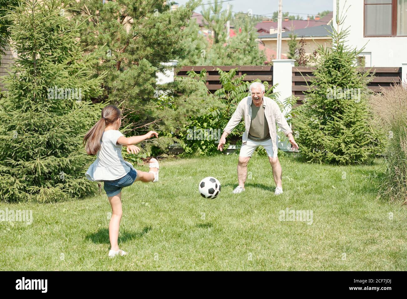 Active senior man playing soccer with his little granddaughter on lawn in backyard, copy space Stock Photo