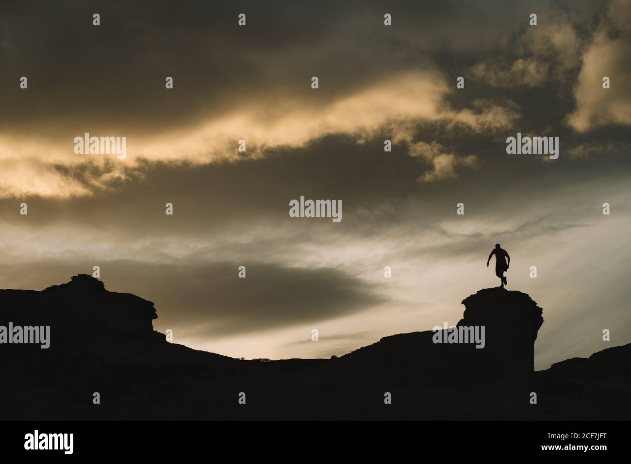 From below of male silhouette in motion on mountain with beautiful cloudy sky on background Stock Photo