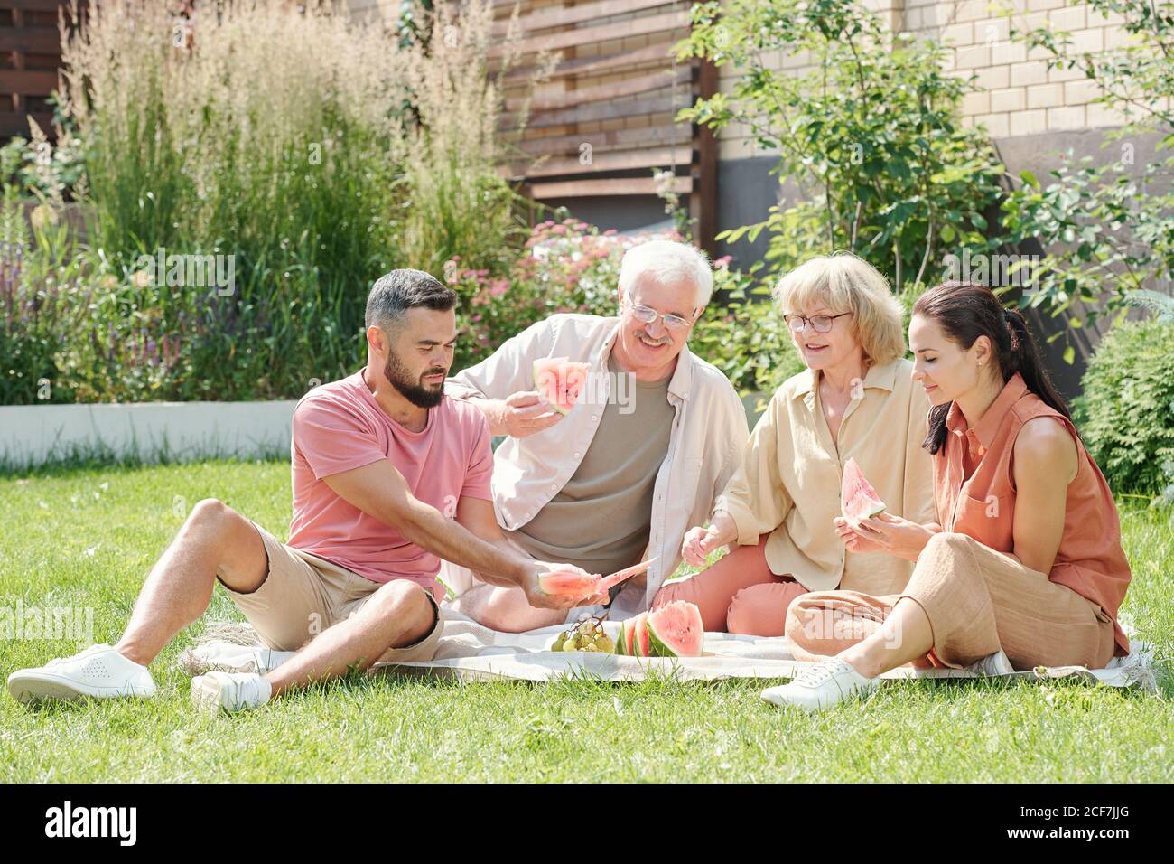 Family shot of senior man and woman having picnic with their young adult children on lawn Stock Photo