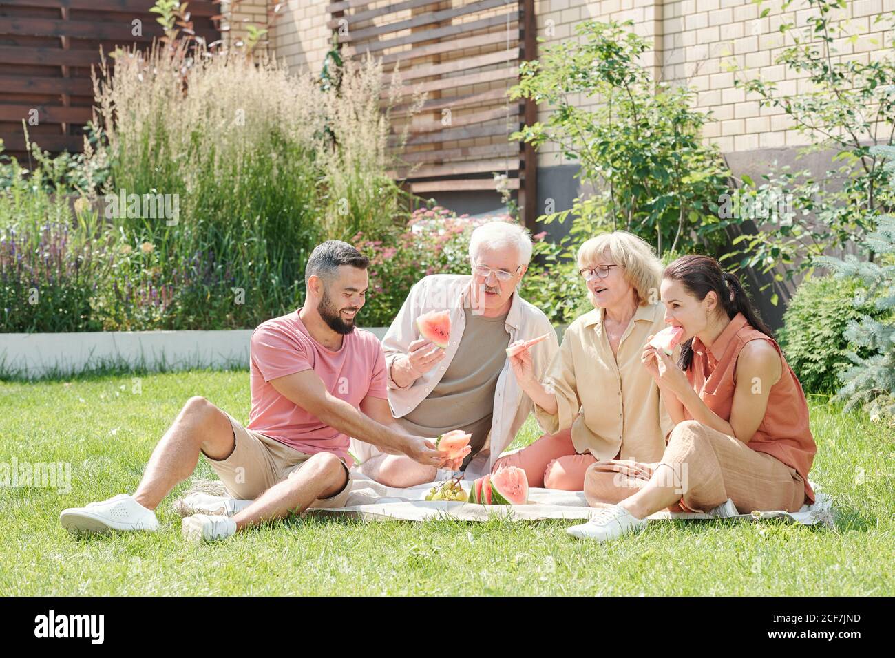 Family shot of modern senior man and woman having picnic with their grown up children on lawn, copy space Stock Photo