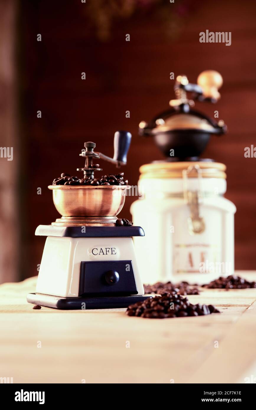Vintage manual mills with coffee beans placed on wooden table in cozy