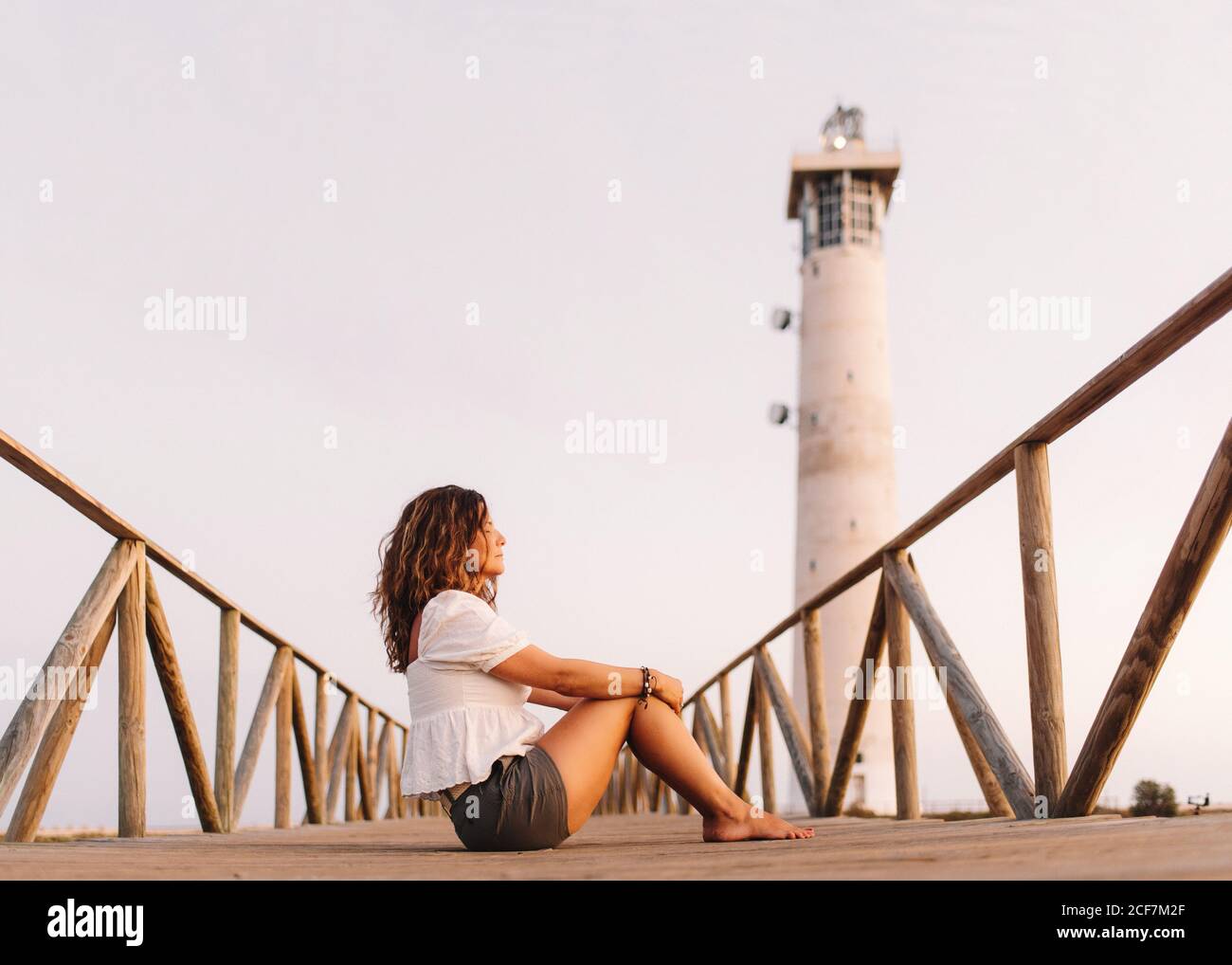 Woman sitting on bridge to lighthouse and looking away Stock Photo