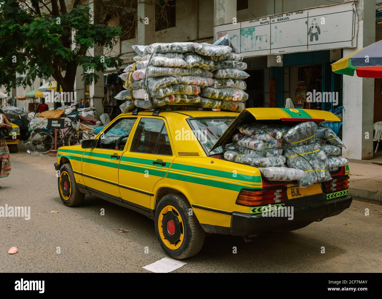 Gambia, Africa - August 5, 2019: Side view of yellow car overloaded with packaged shoes on roof and in trunk for selling in shop during transportation on village Stock Photo