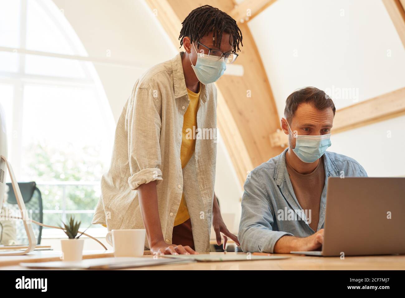 Software developers in protective masks using laptop in work they developing new program Stock Photo
