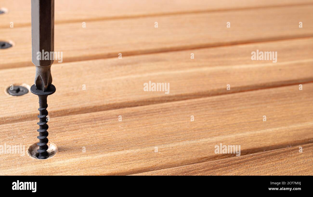 The screwdriver twists the self-cut into wooden boards. Construction tools, home repairs. Stock Photo