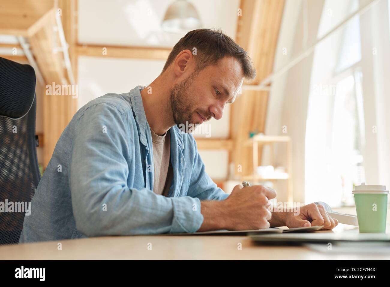 Serious mature businessman sitting at the table and writing he doing paperwork at office Stock Photo
