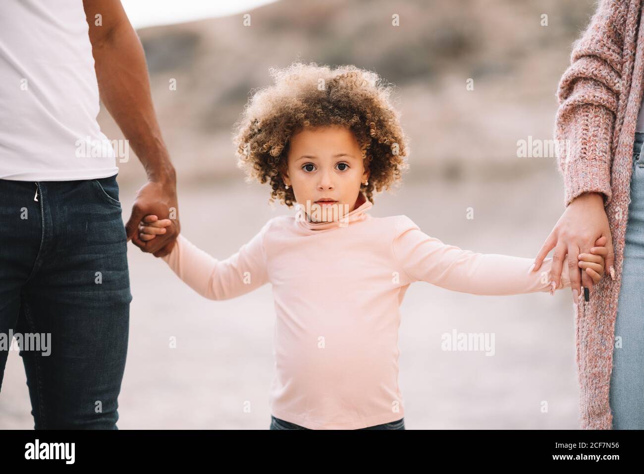 Cropped unrecognizable diverse mother father and curly child wearing bright casual clothes strolling on nature holding hands at daytime Stock Photo