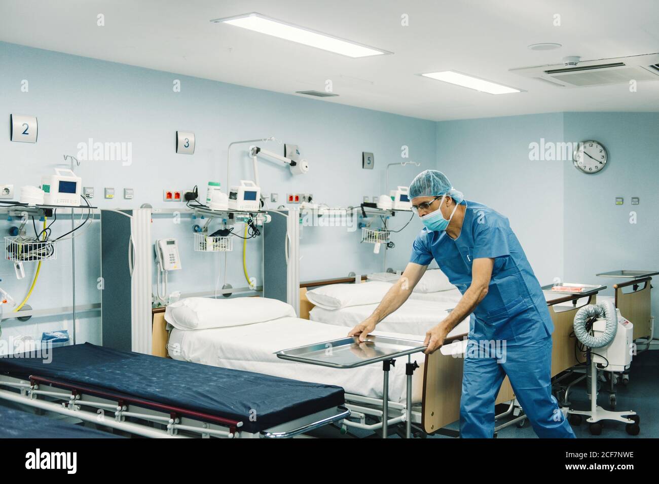 Medic in blue uniform and protective mask setting tray on trolley in
