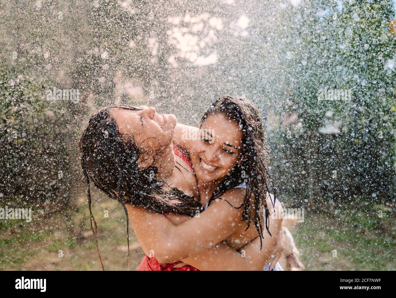 Friends in swimsuits hugging under water drops Stock Photo