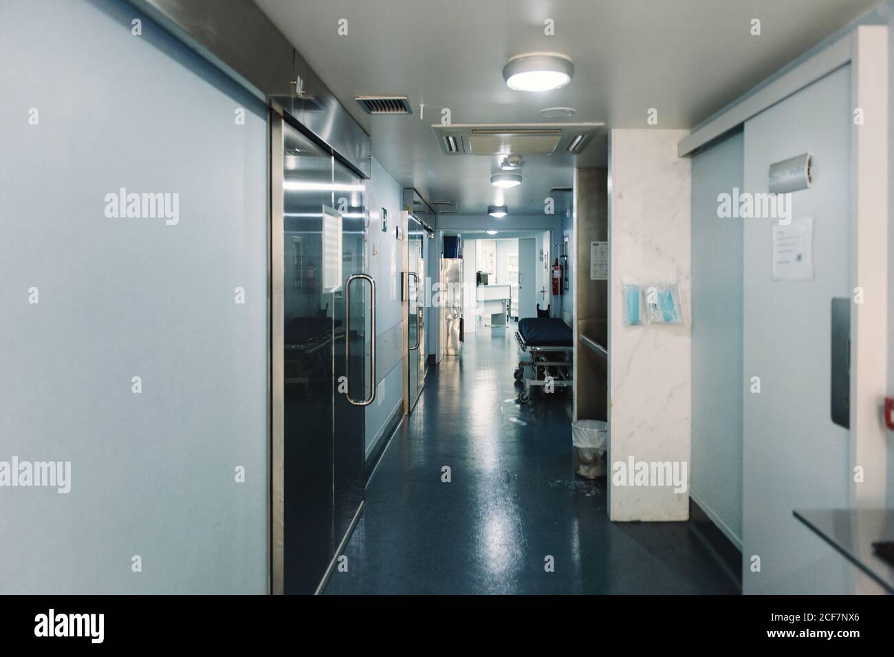 Deserted corridor in clinic with empty hospital trolley and lights on Stock Photo