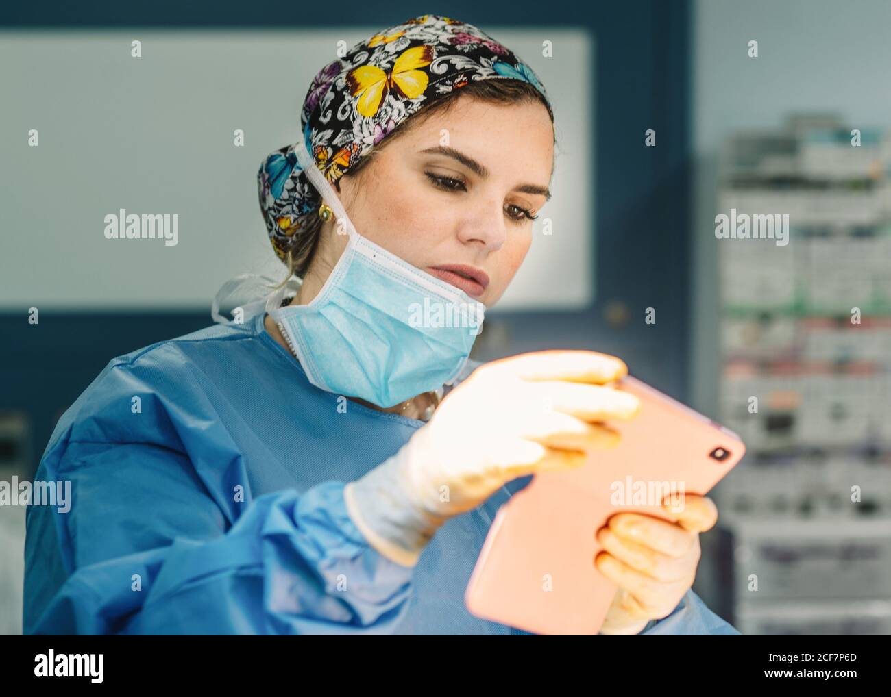 Beautiful Woman in surgical gown and mask taking photo and using mobile phone during operation Stock Photo