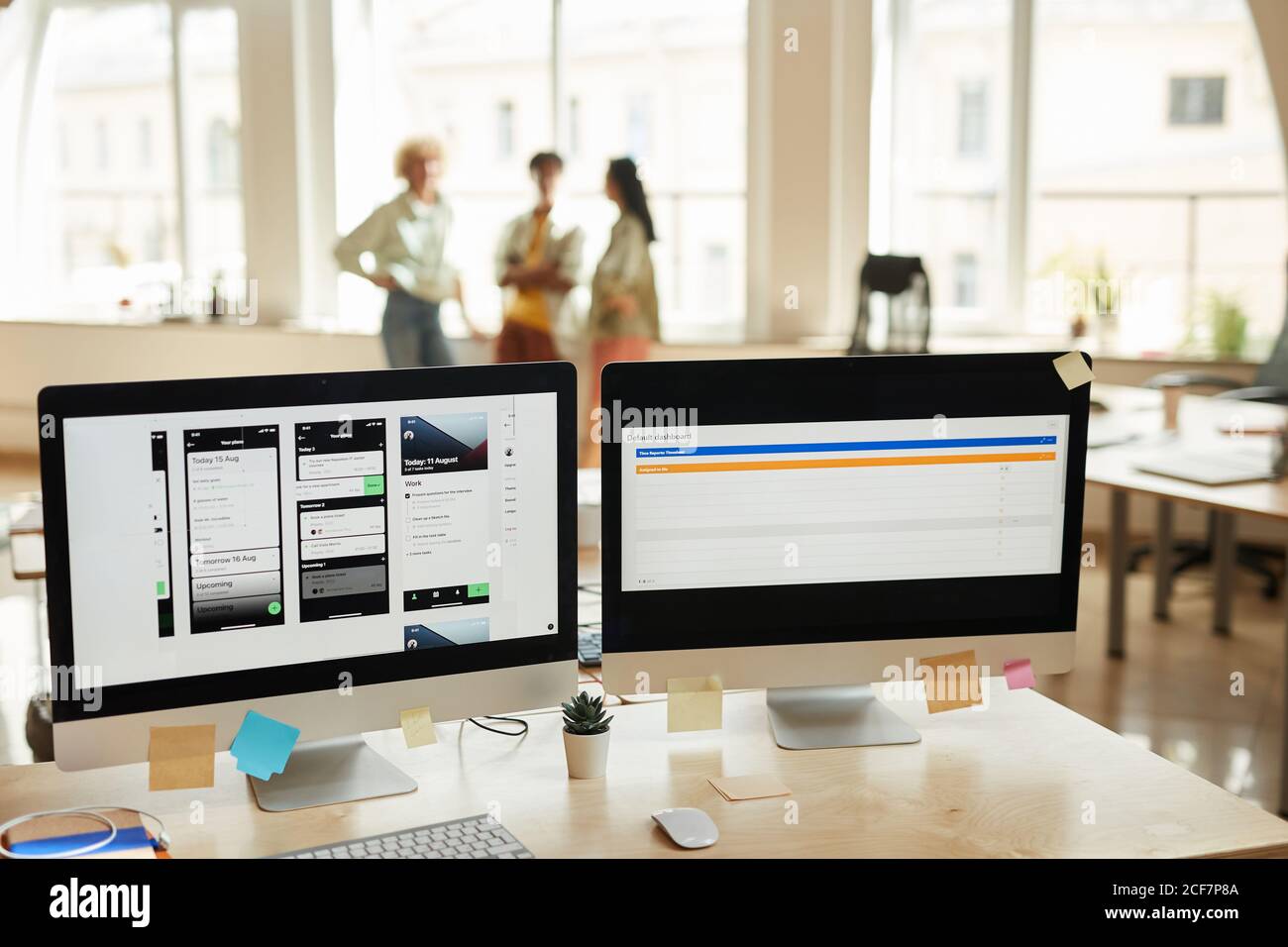 Image of computer monitors with new software on the table at office with people working in the background Stock Photo