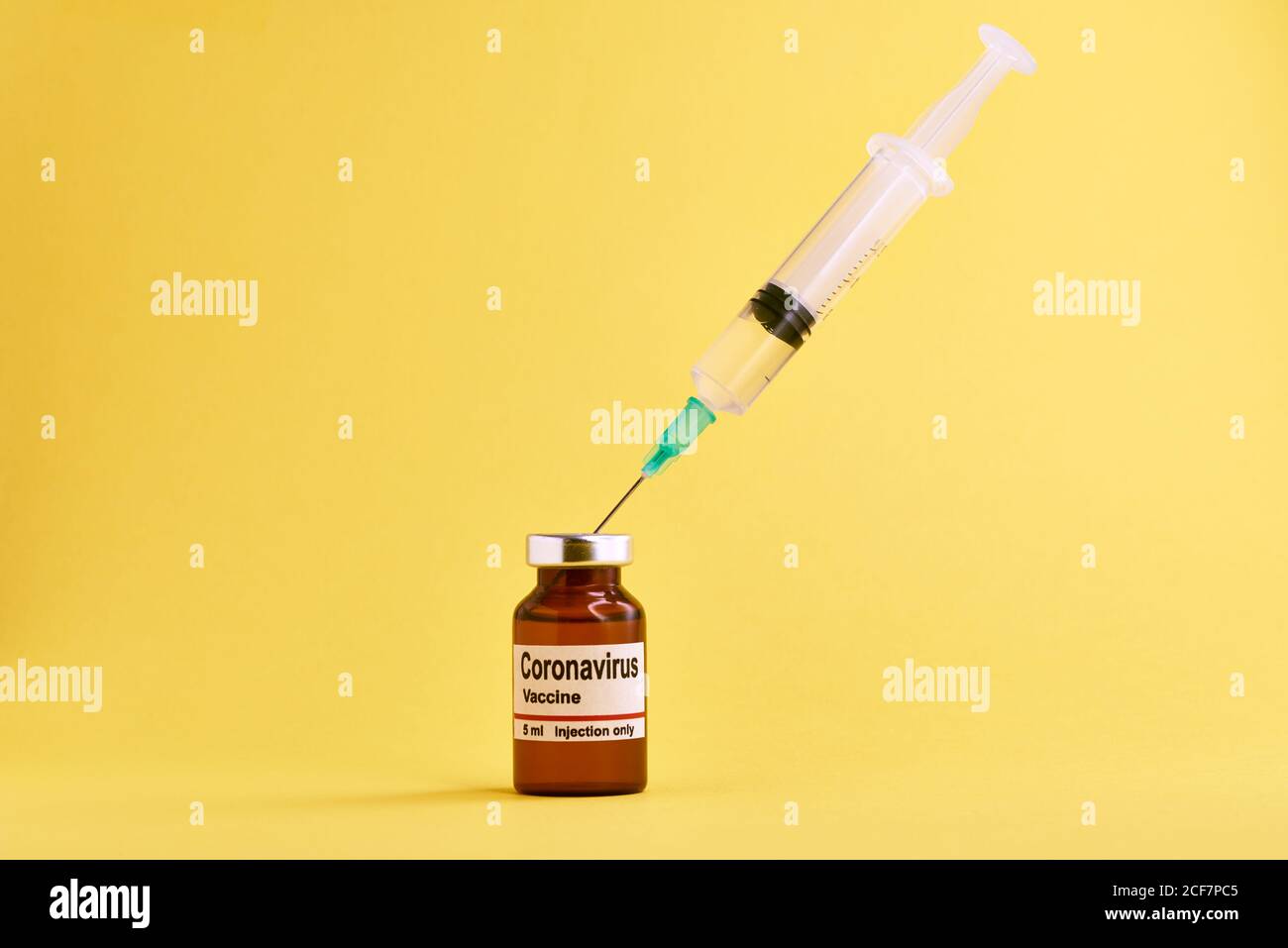 Medical syringe and glass vial with coronavirus vaccine placed against yellow background Stock Photo