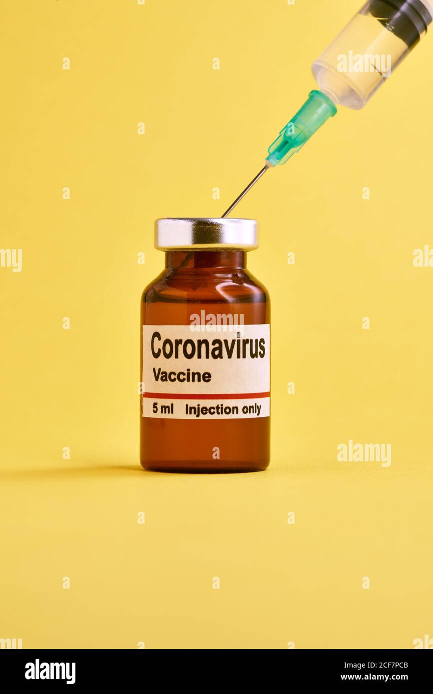 Medical syringe and glass vial with coronavirus vaccine placed against yellow background Stock Photo