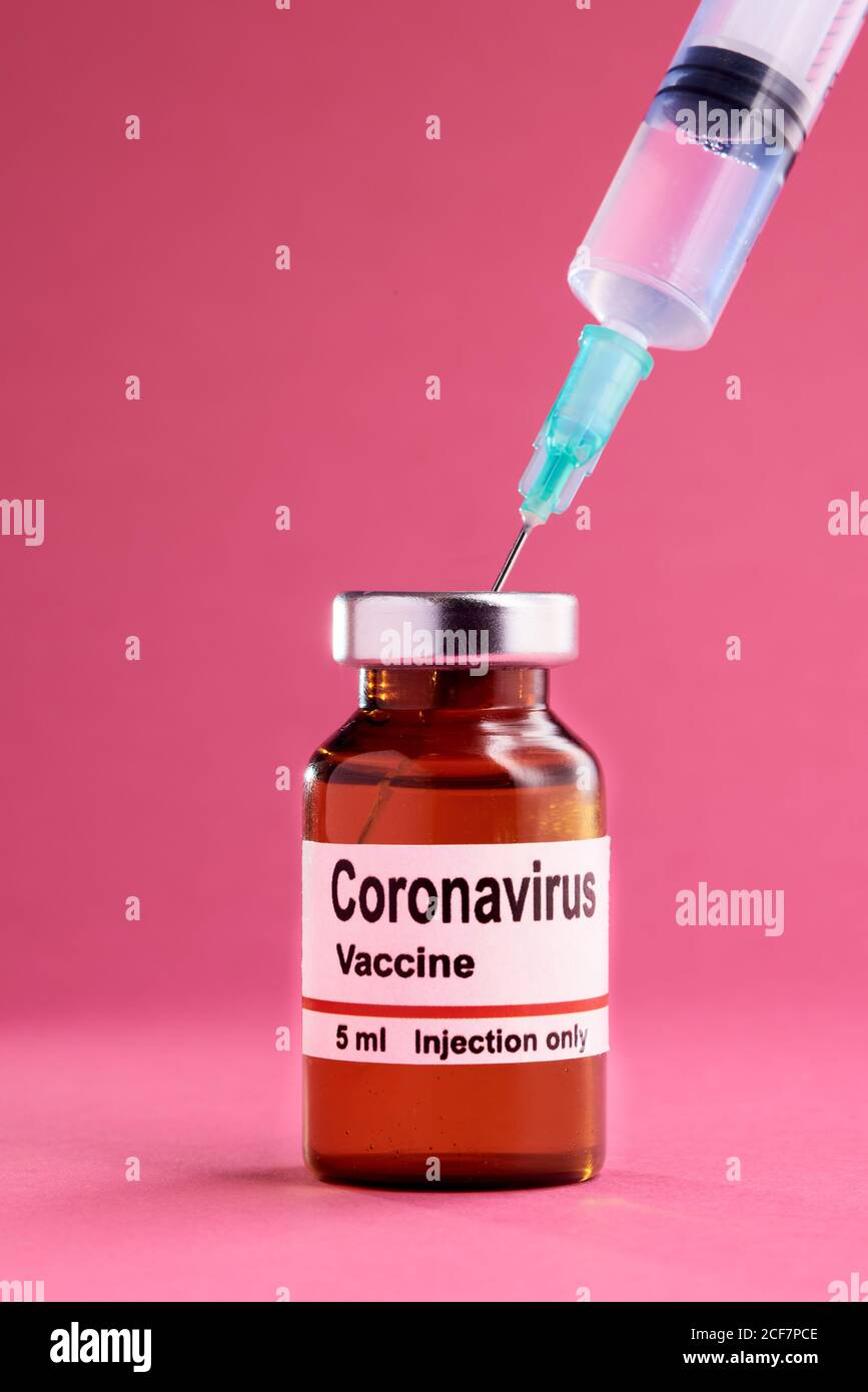 Medical syringe and glass vial with coronavirus vaccine placed against pink background Stock Photo