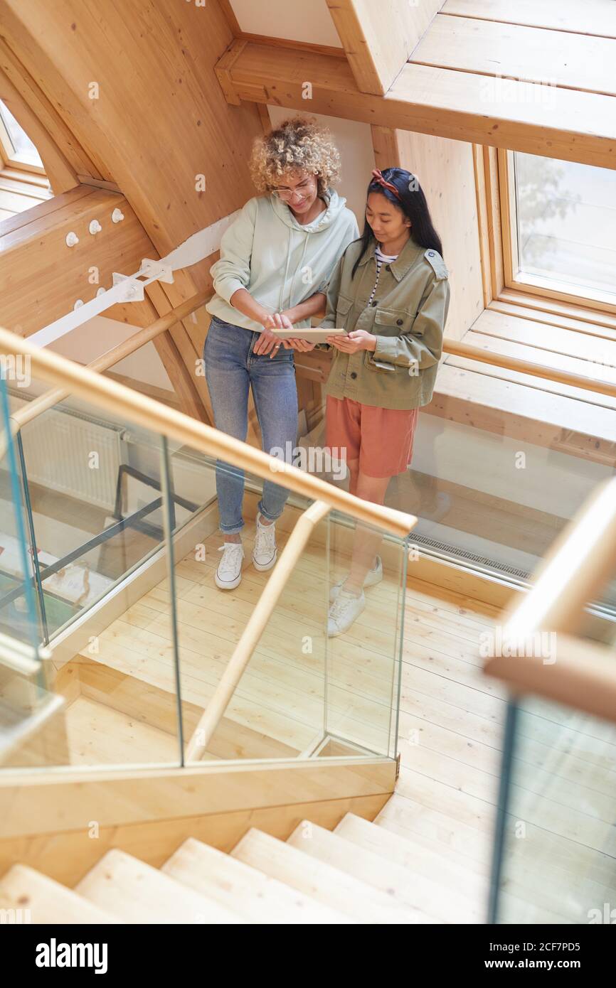 Two colleagues using digital tablet together while standing on wooden staircase Stock Photo