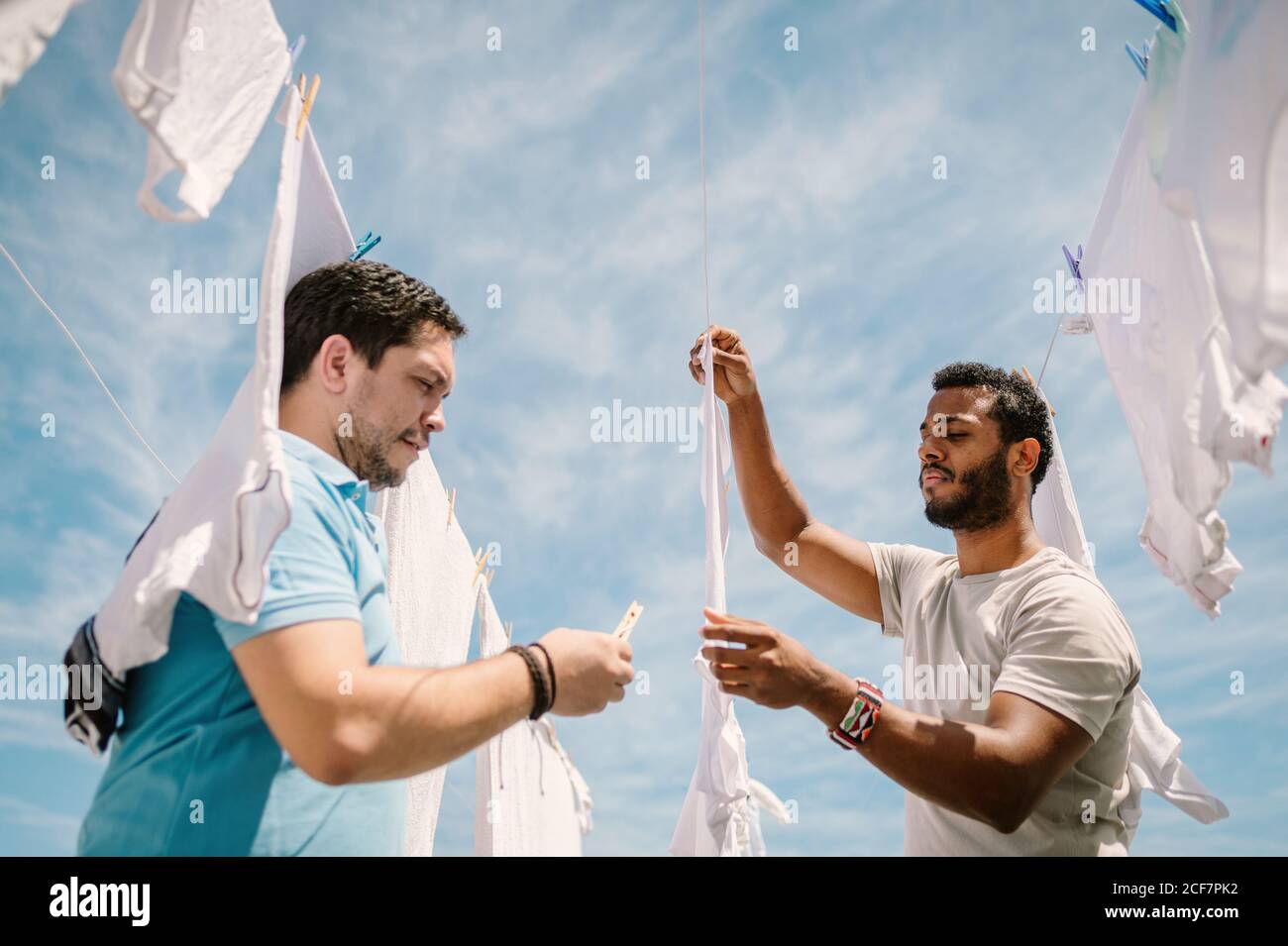Multiracial men hanging clothes in bright day Stock Photo