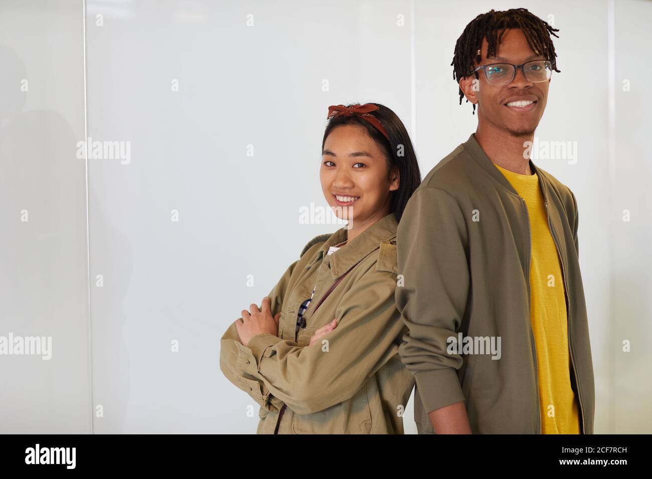 Portrait of multiethnic young couple standing back to back and smiling at camera against the white background Stock Photo