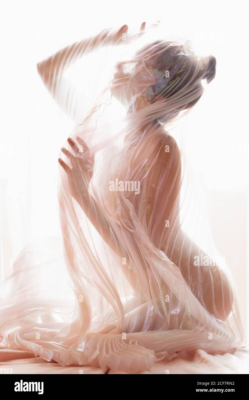 Side view of anonymous naked model covered with transparent pleated fabric  of curtain against bright sunlight Stock Photo - Alamy