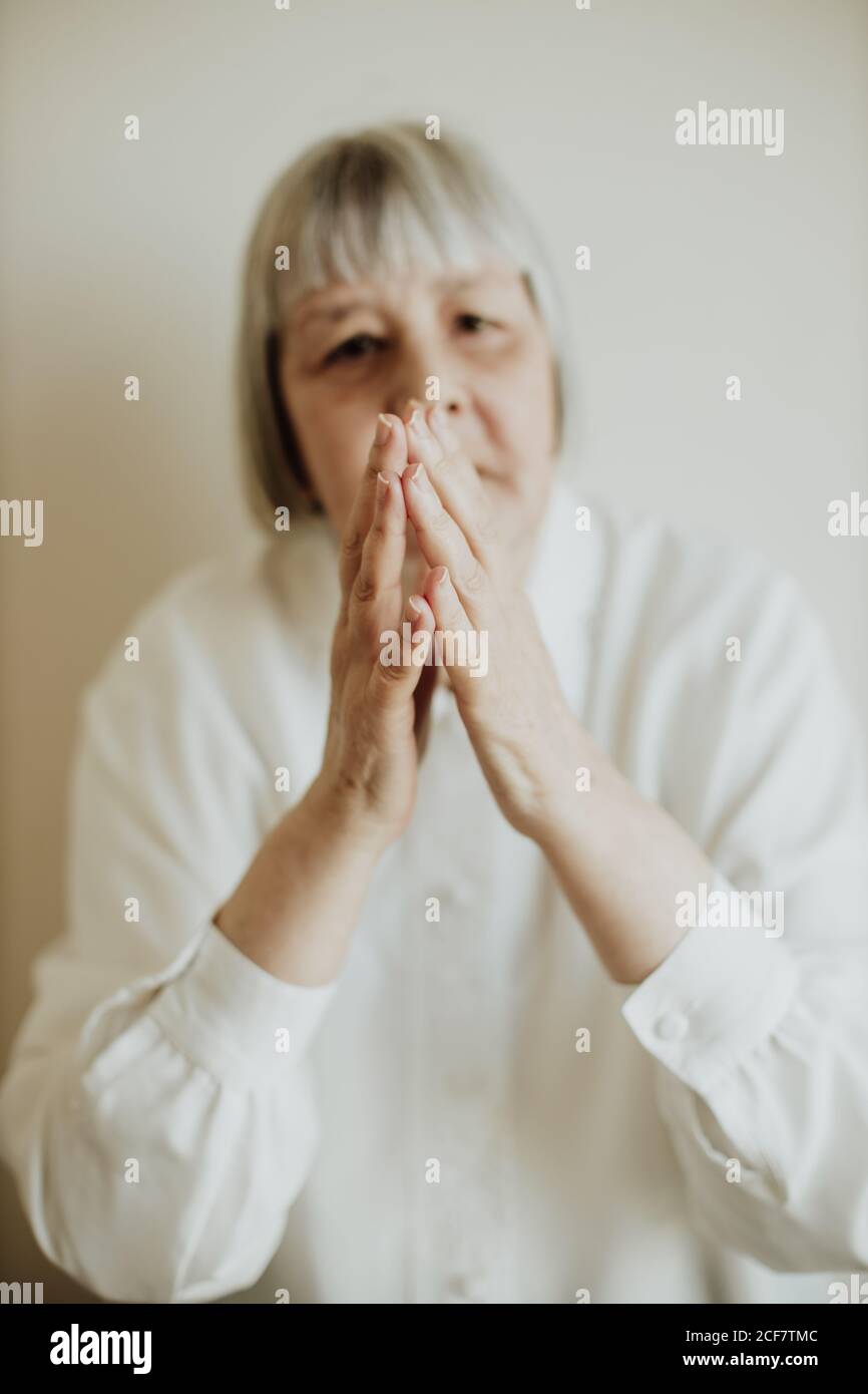 Sad elderly Woman in white blouse showing disagreement while rising hands up on light background looking at camera Stock Photo