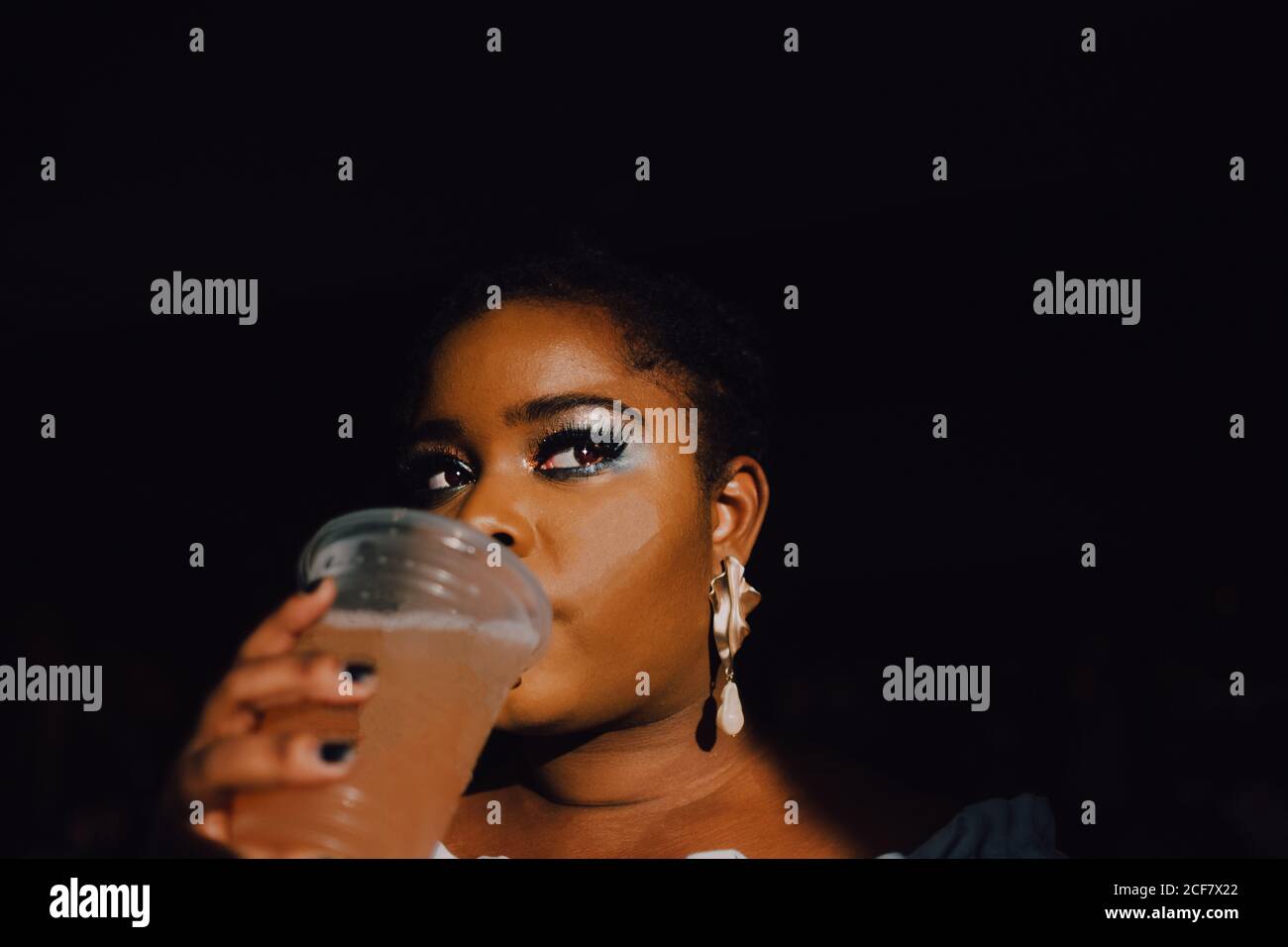From below portrait of backlit beautiful curvy black young Woman with bright make-up in off-shoulder dress having a cold beverage drink Stock Photo