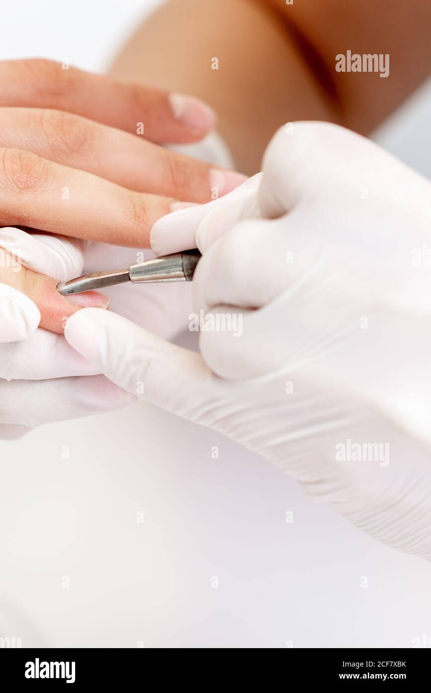 Hands of manicurist pushing cuticles on female's nails with manicure