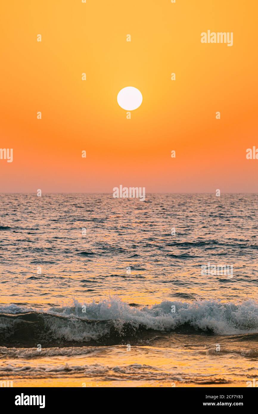 Sunset Sun Shine Above Sea. Natural Sunrise Sky Warm Colors Over Ripple Sea. Ocean Water Foam Splashes Washing Sandy Beach Stock Photo