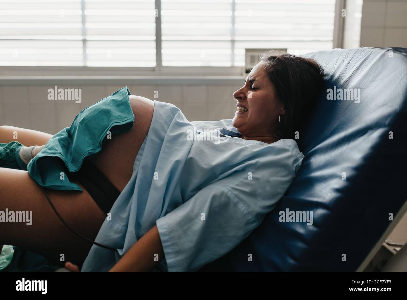 Strained female grasping handle and grunting in pain while giving birth to baby on medical chair in modern hospital Stock Photo