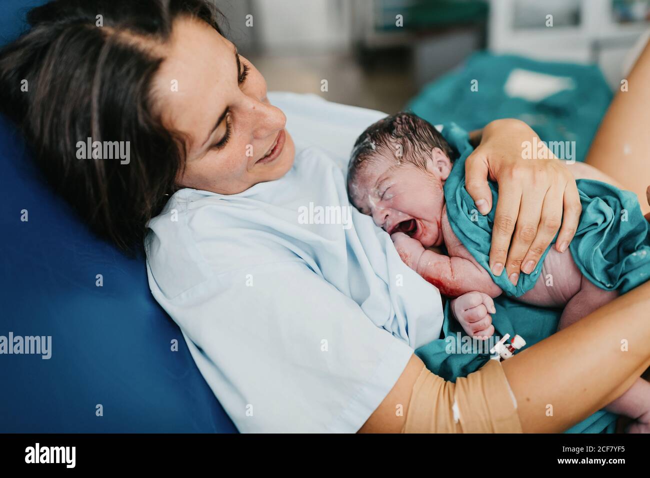 High angle of cheerful adult Woman embracing newborn child covered with