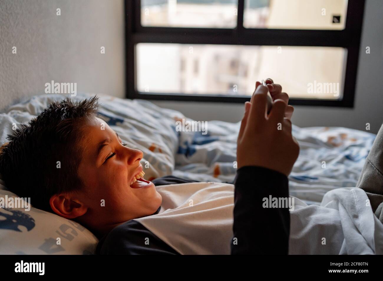 Delighted boy using tablet in bedroom during weekend Stock Photo