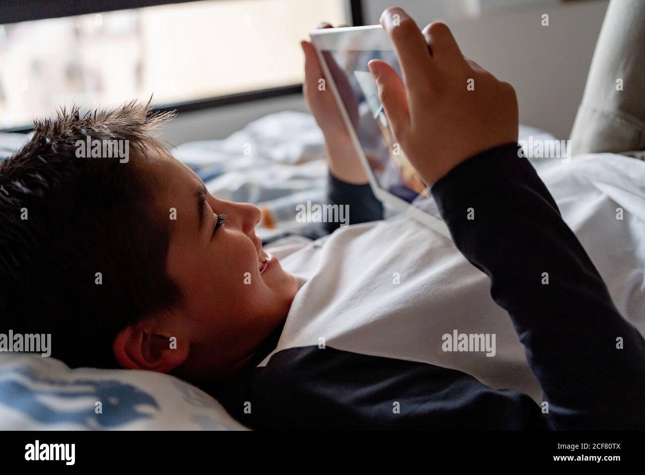 Delighted boy using tablet in bedroom during weekend Stock Photo
