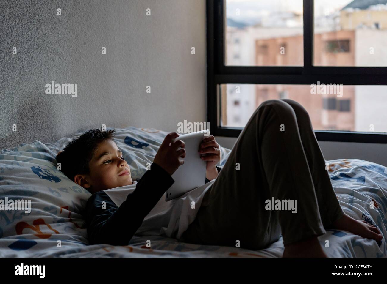 Delighted boy using tablet in bedroom during weekend Stock Photo