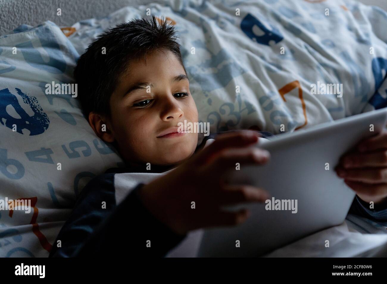 Delighted boy using tablet in bedroom during weekend Stock Photo