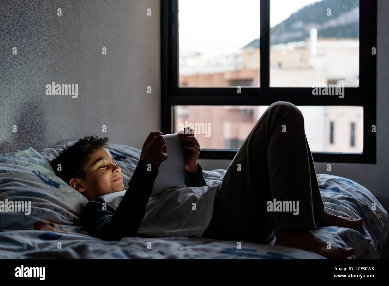 Delighted boy using tablet in bedroom during weekend Stock Photo