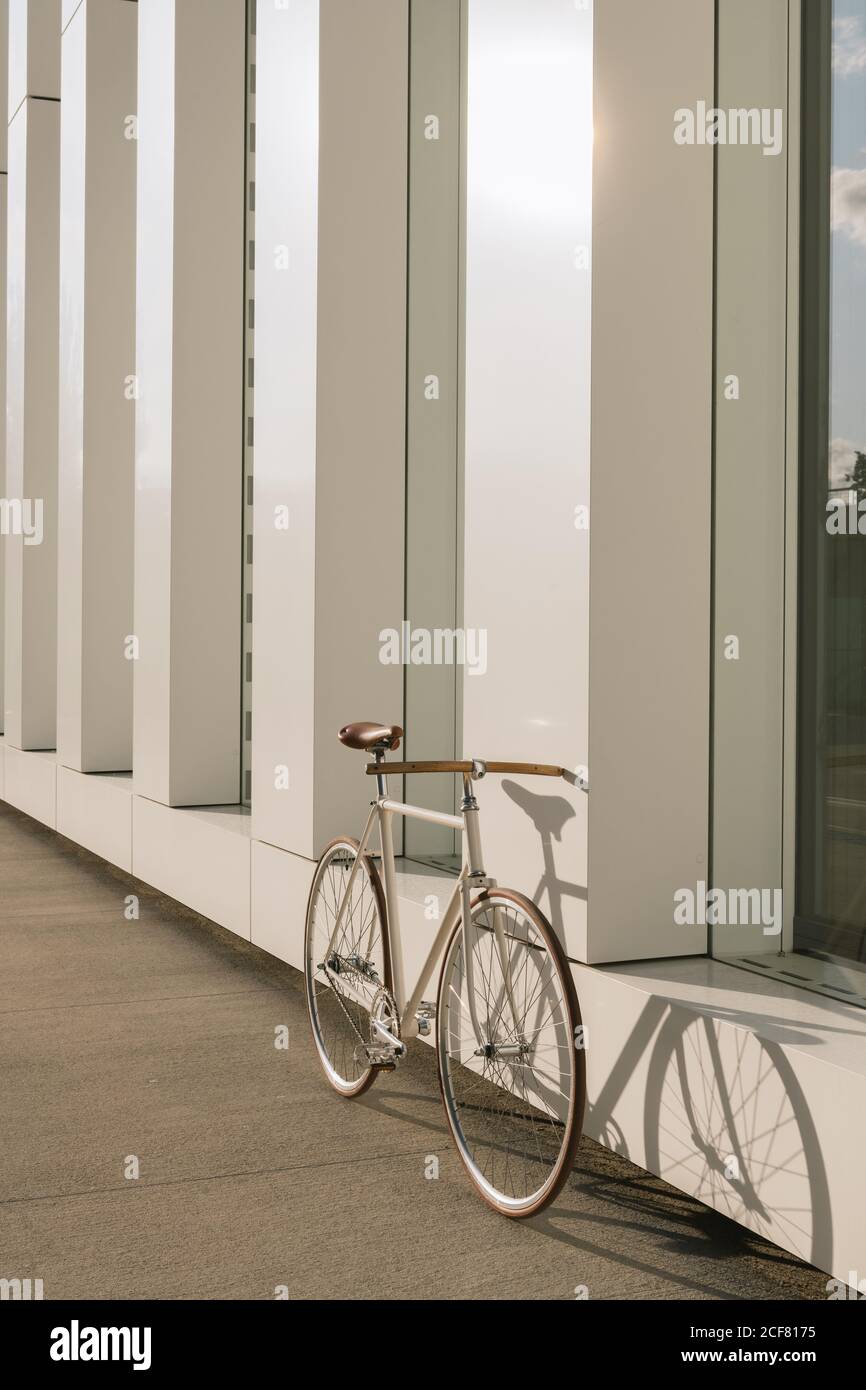 Bike parked on sidewalk near wall of contemporary building on sunny day on city street Stock Photo