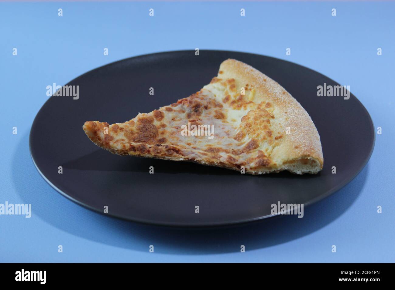 Dried slice of pizza on a black table on a blue background. Food concept. Stock Photo