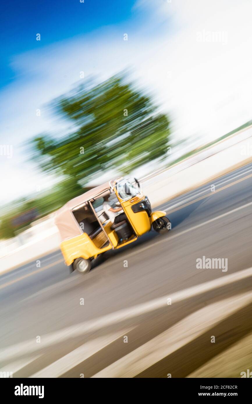 Blurred yellow three wheeler riding fast on paved roadway in sunlight