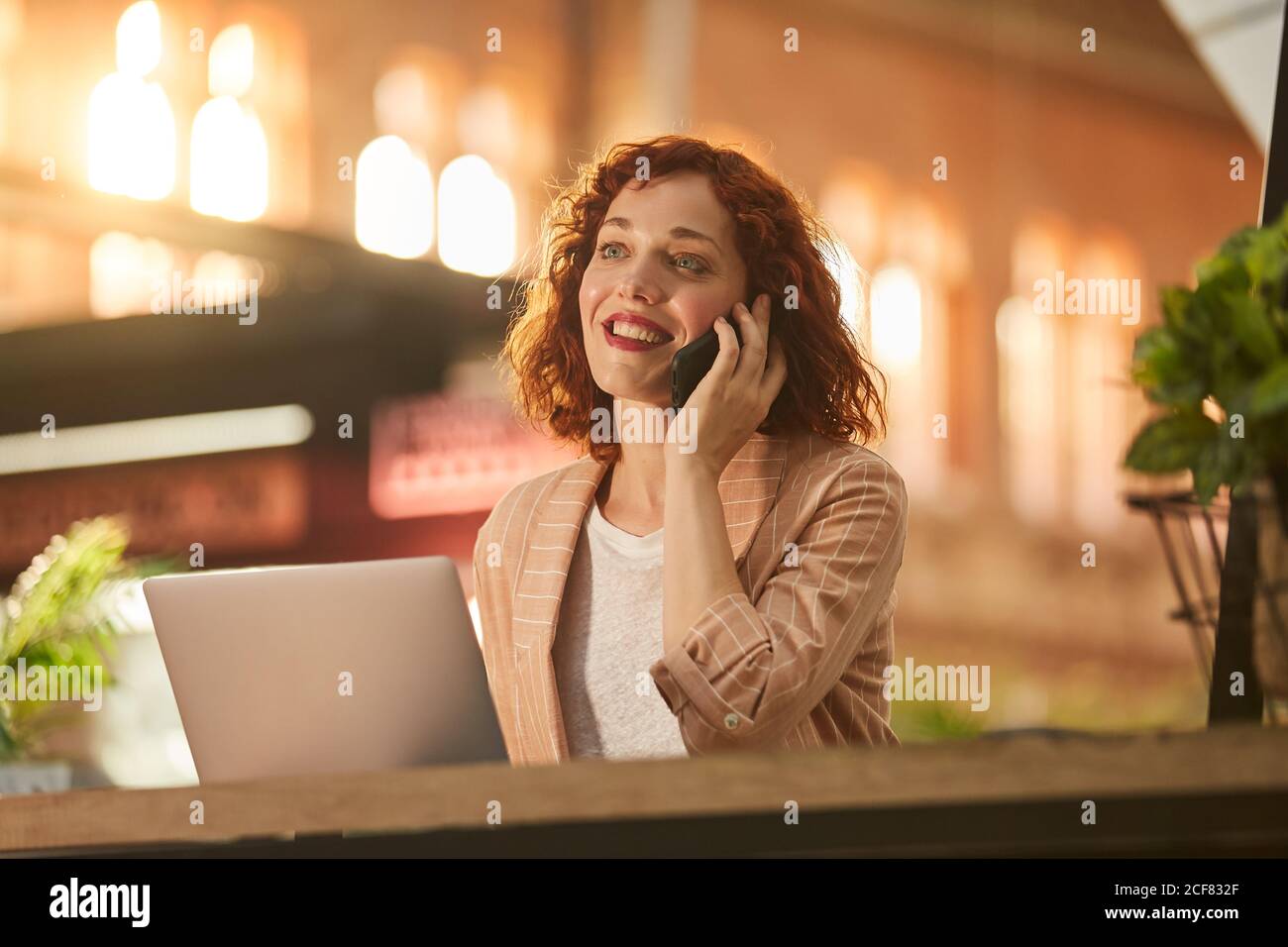 Young Woman talking on phone while working on laptop Stock Photo