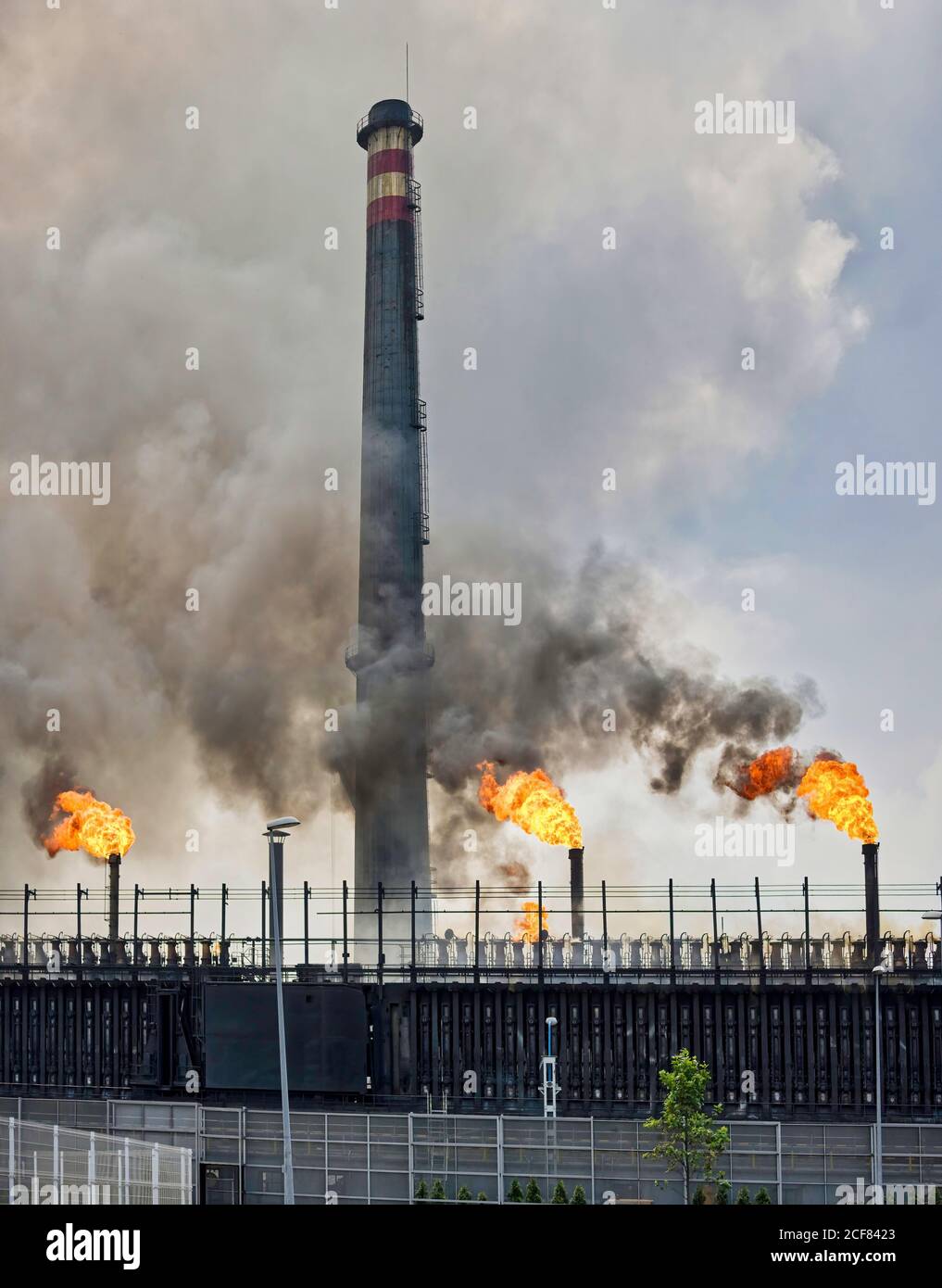 Weathered industrial buildings and pipes emitting smoke and flames at coking factory Stock Photo