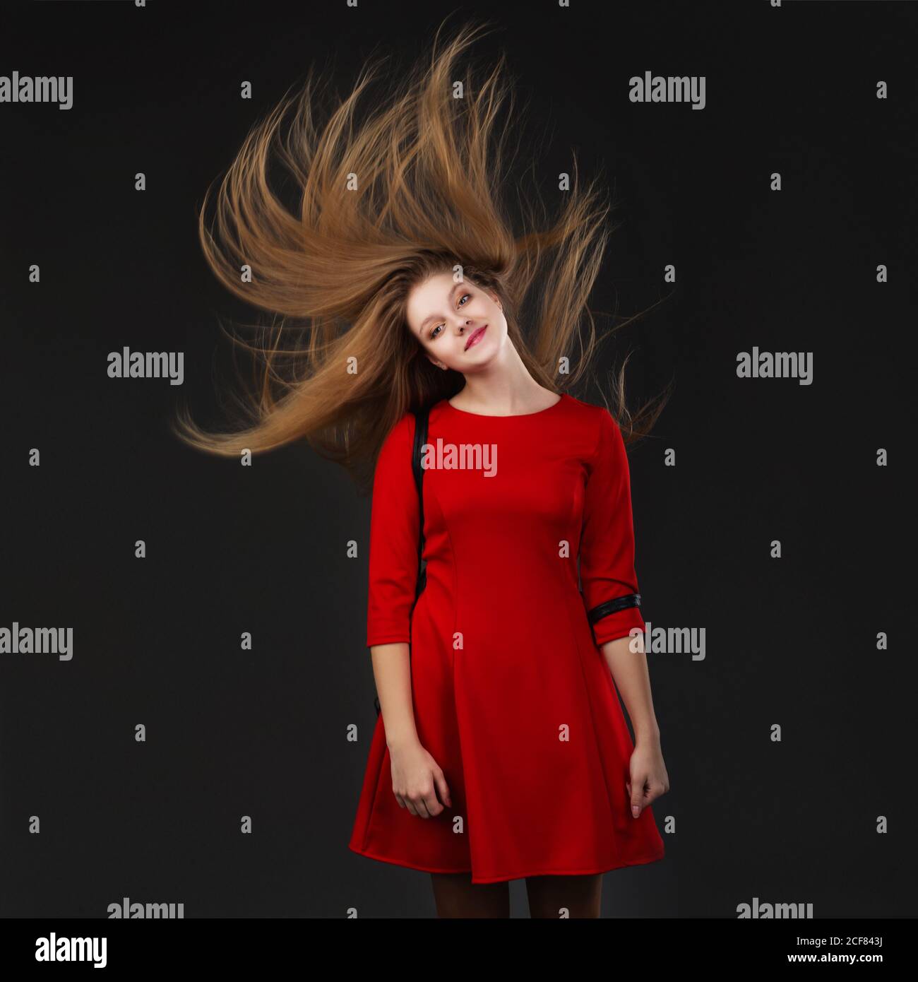 Portrait of a smiling young beautiful girl in a red dress with a flying ...