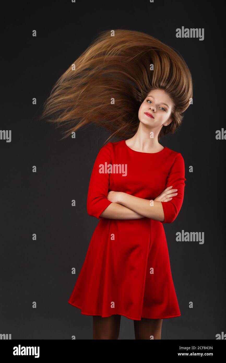 Portrait of a smiling young beautiful girl in a red dress with a flying ...