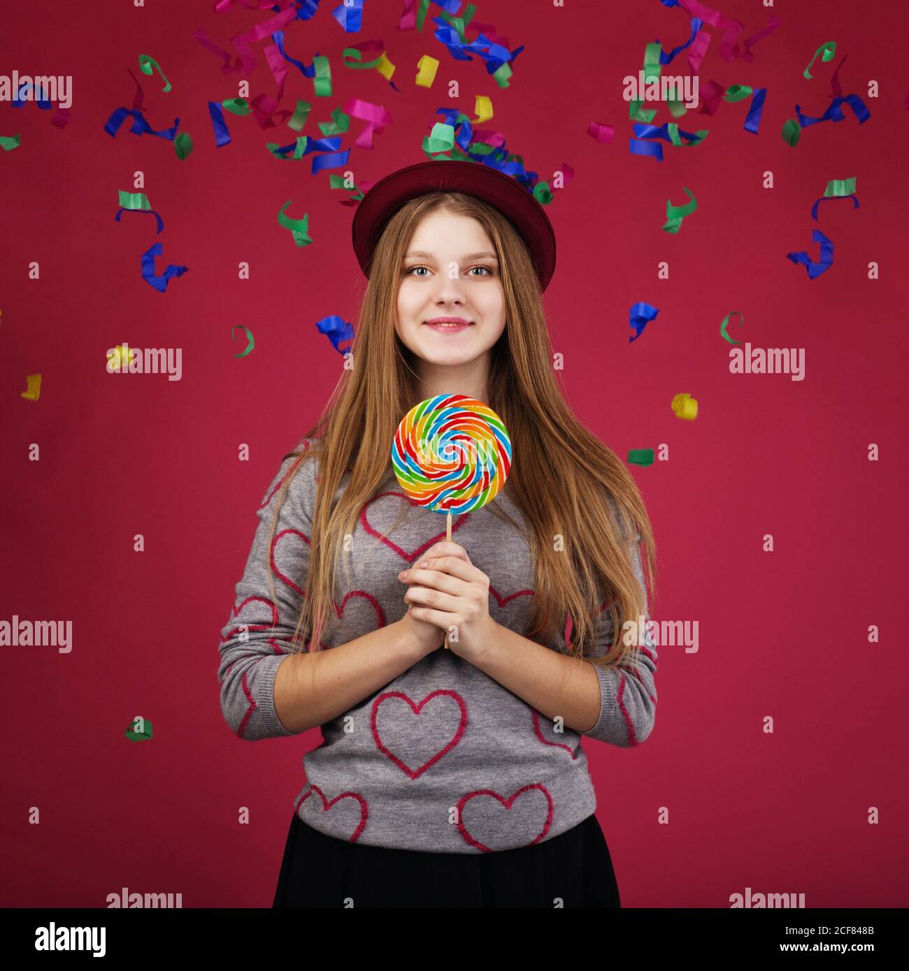 Portrait of a teen girl throws up a multi-colored tinsel and confetti. beautiful girl wearing hat holding big striped lollipop Stock Photo